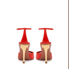 Rear profile of the red coral Kara sandal, emphasizing the slender ankle strap fastening and the base of the sculptural golden Clepsydra heel