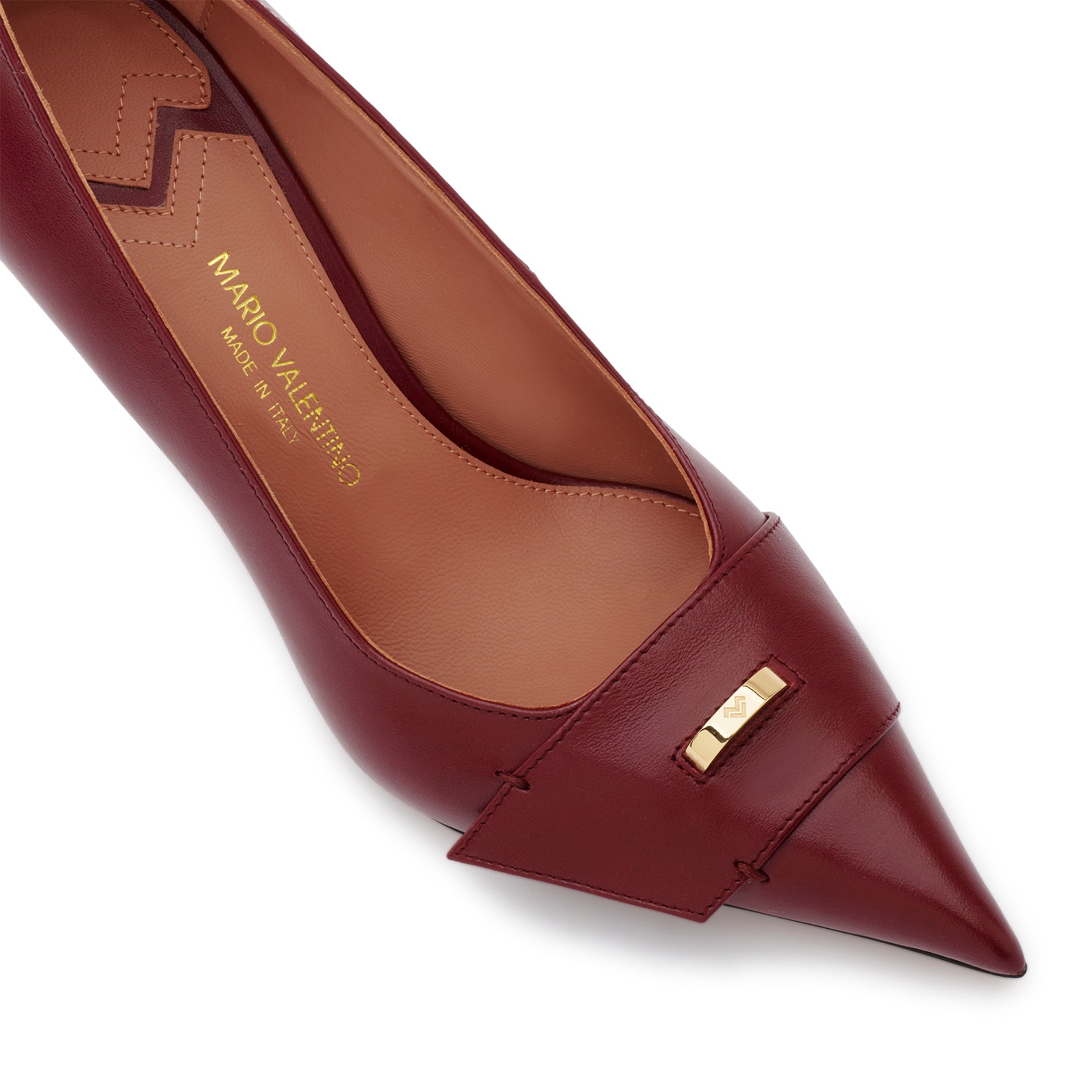 Detail of burgundy calfskin pumps with pointed toe and gold logo ring accessory